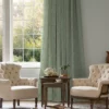 green floral curtains at a window with 2 cream armchairs in front. A wooden table with a tea set in between.
